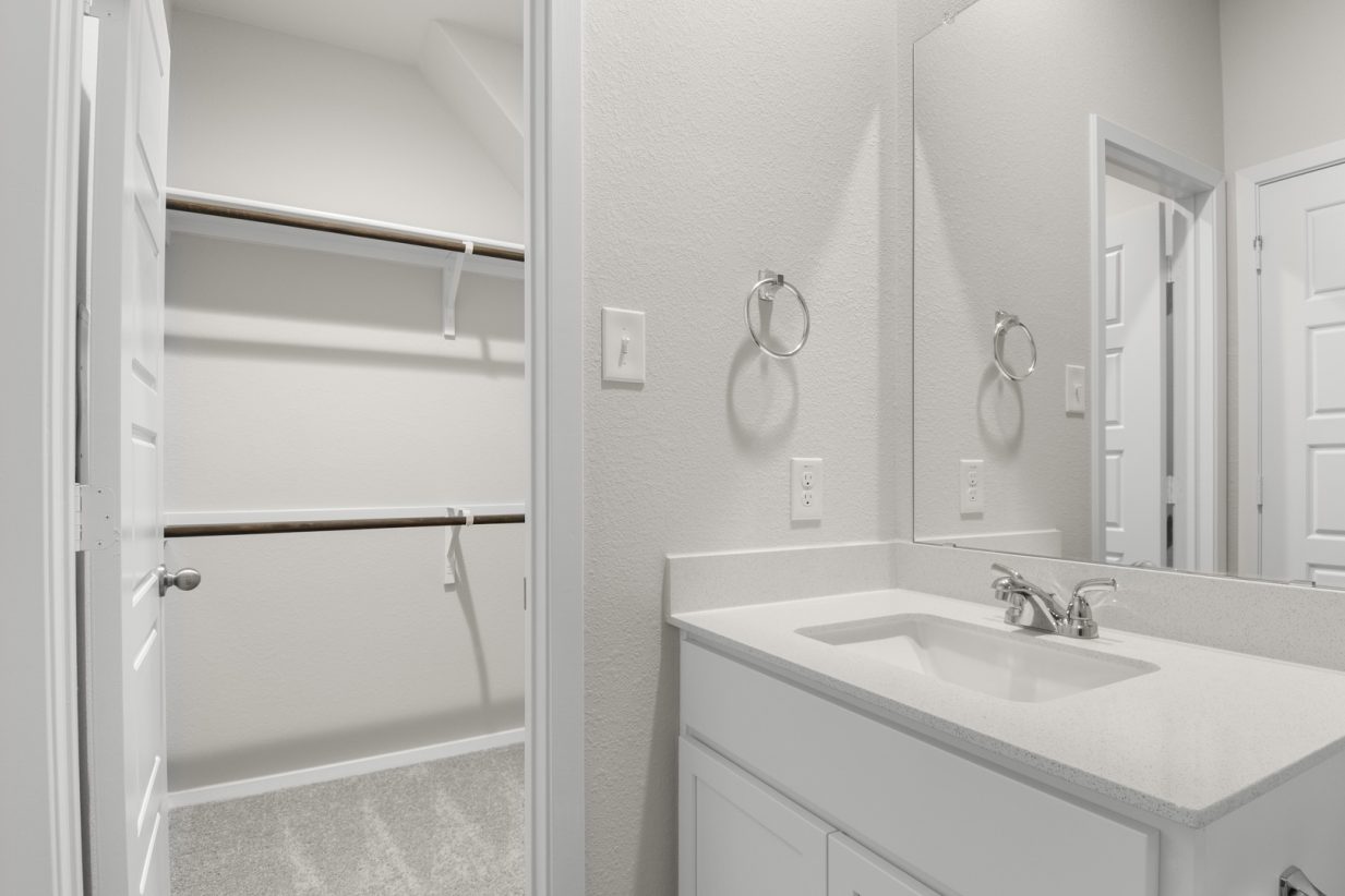 Image of primary bathroom with white cabinets and mirror with vanity and a walk in closet