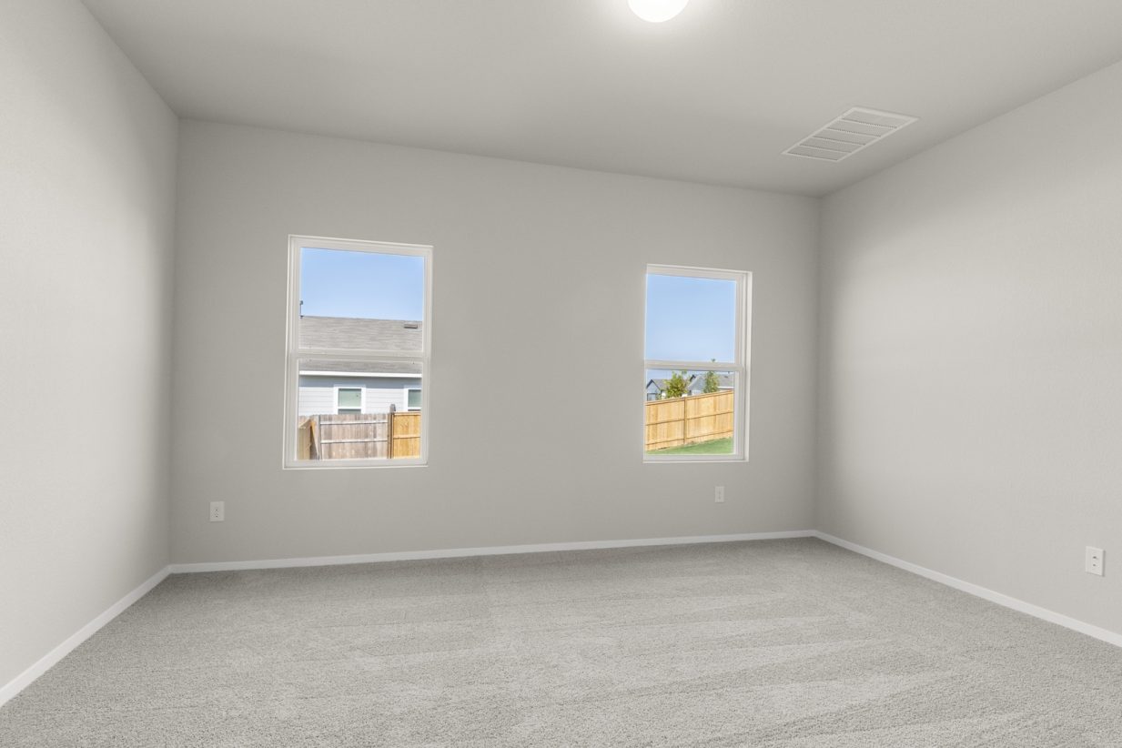 Image of a primary bedroom with tan carpeting, cream walls, windows and white trim