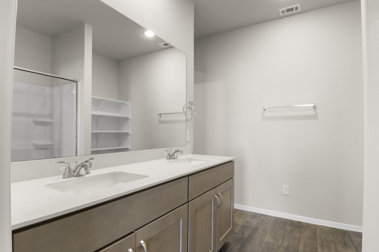 Image of a primary bathroom with a double white vanity, brown cabinets and a large mirror