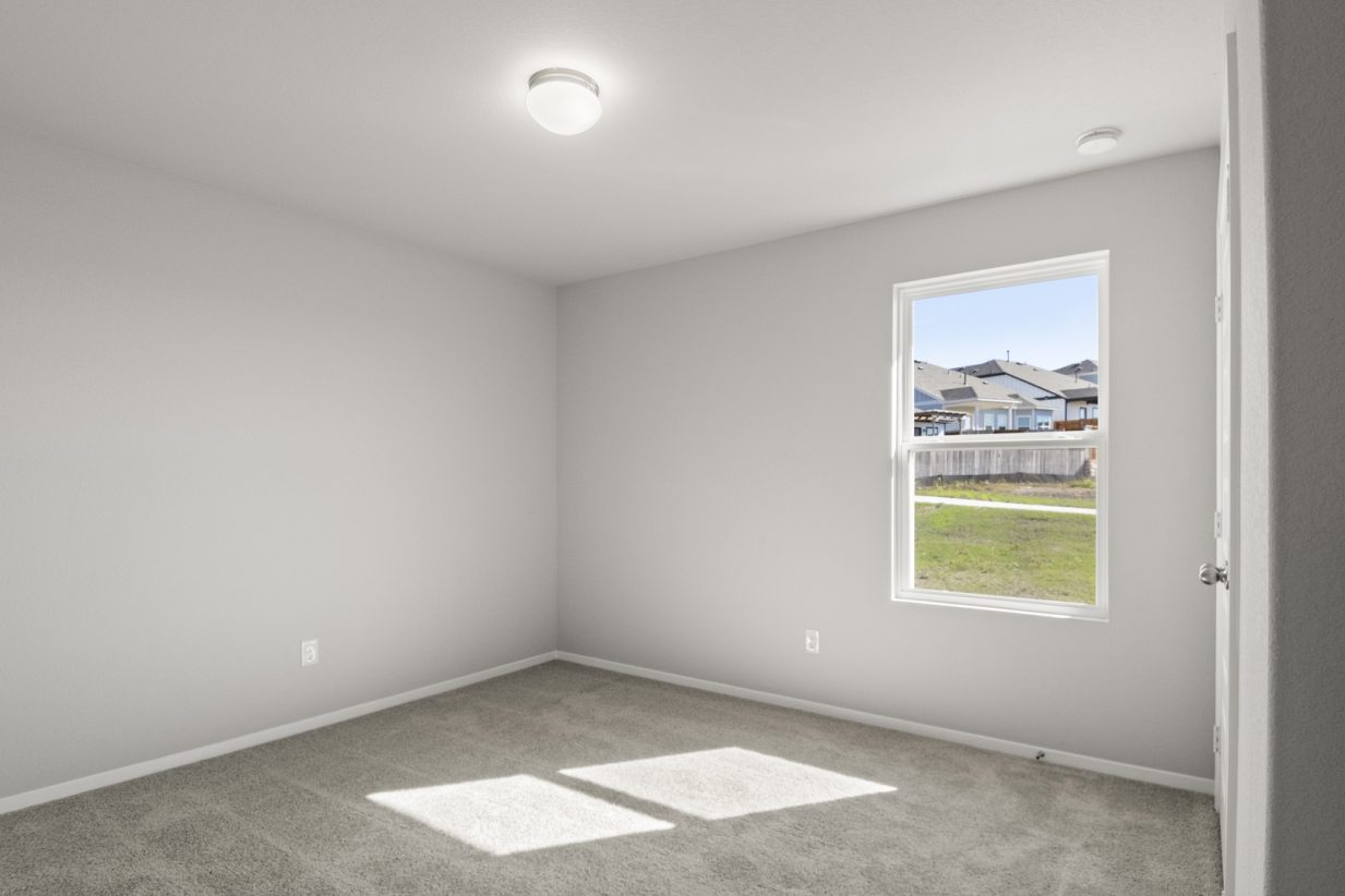 Image if a bedroom with tan carpeting and light grey painted walls with a window