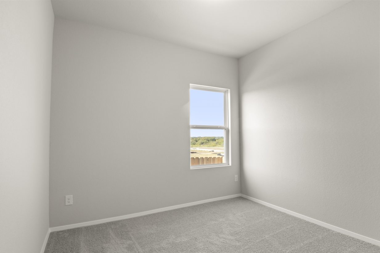 Image of a bedroom with tan carpeting and light grey walls with a window