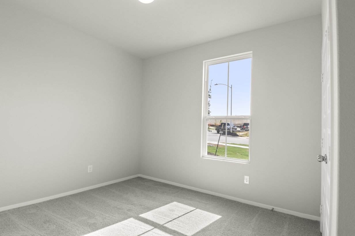 Image of a bedroom with tan carpeting and light grey walls with a large winow