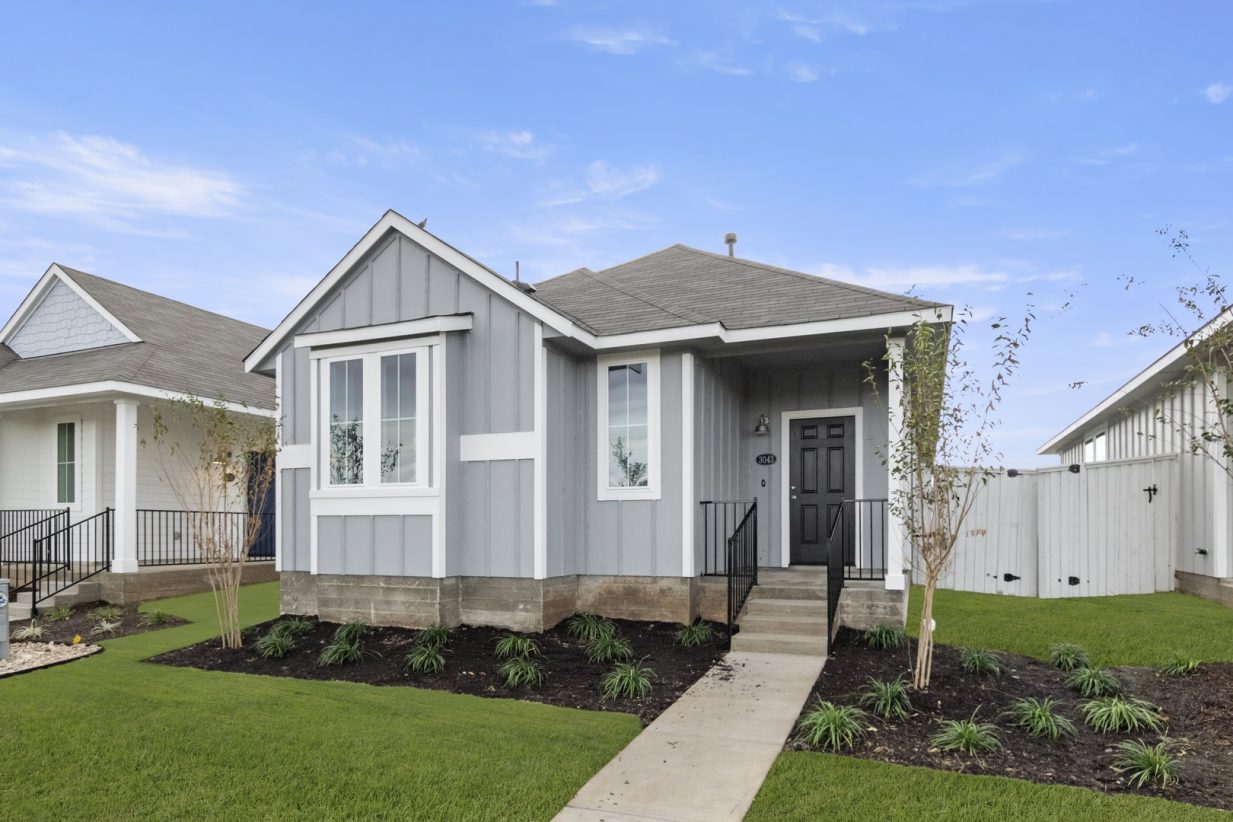 Image of exterior of a one bedroom grey home with a black door and green grass with a blue sky