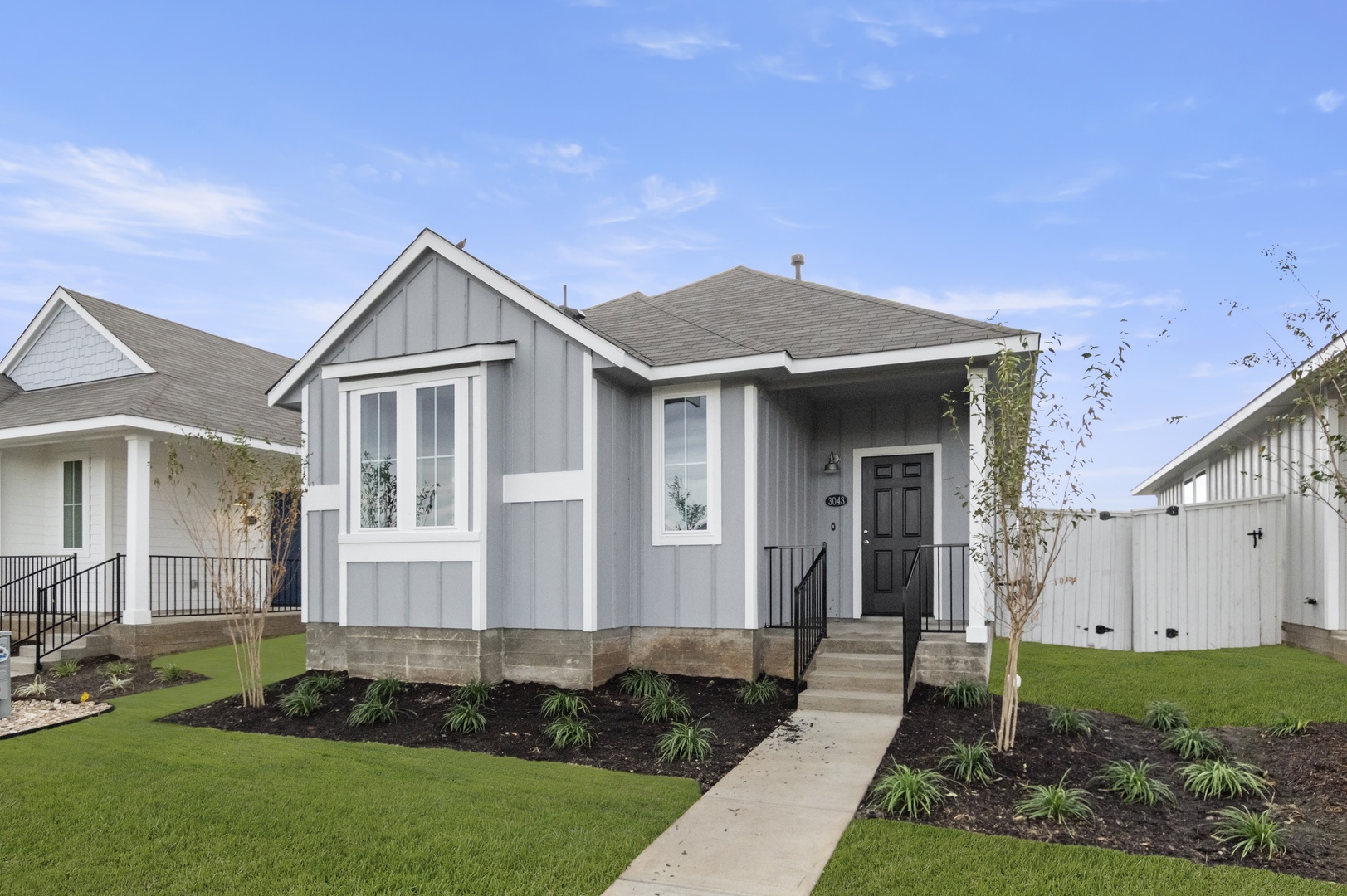 Image of exterior of a one bedroom grey home with a black door and green grass with a blue sky