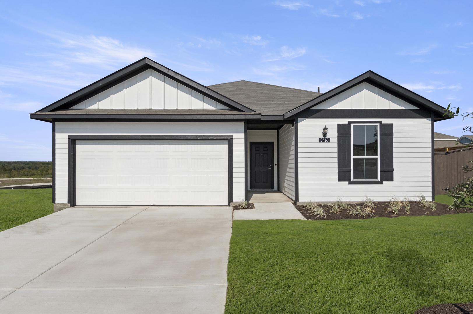 Image of the front exterior of a one story white home with black trim, a black front door, a white garage door and a green grass front yard with a blue sky