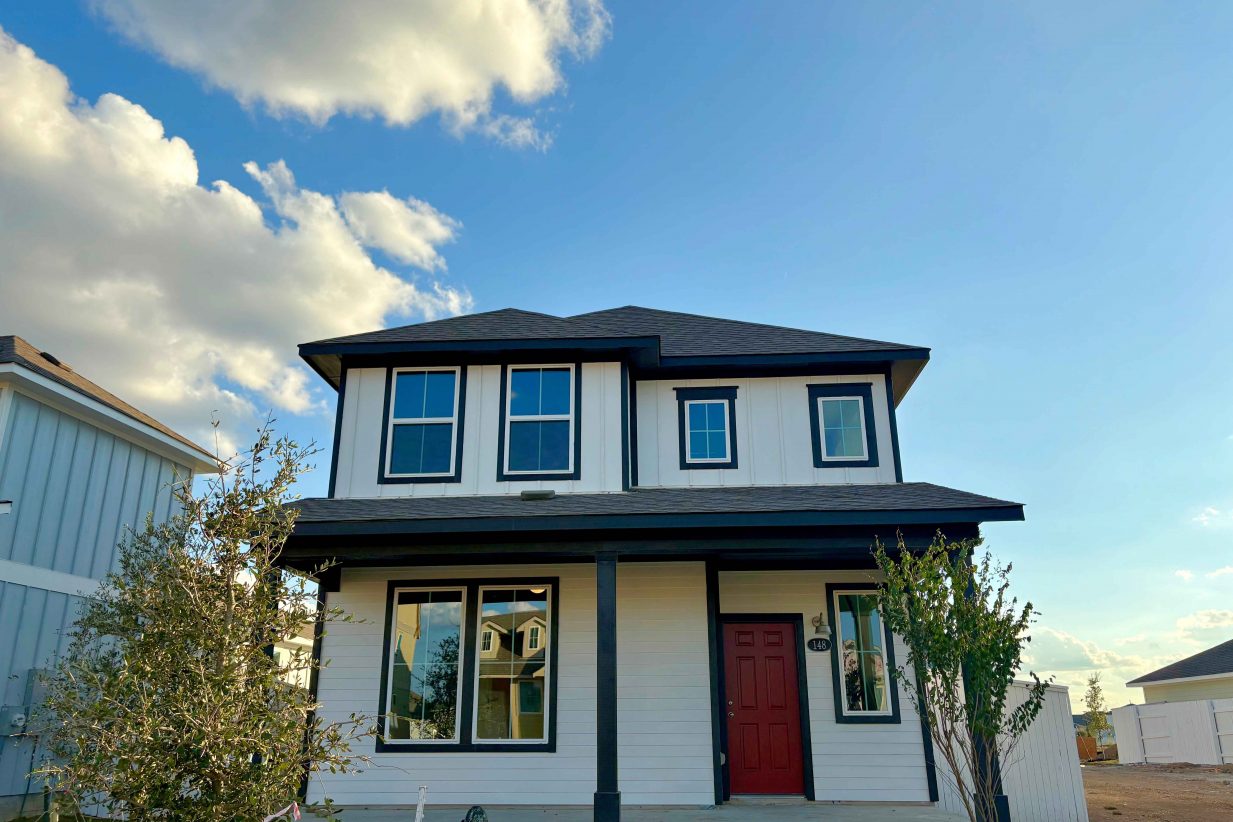 Image of the front of two-story white home framed with black with a red front door and the blue sky with clouds.