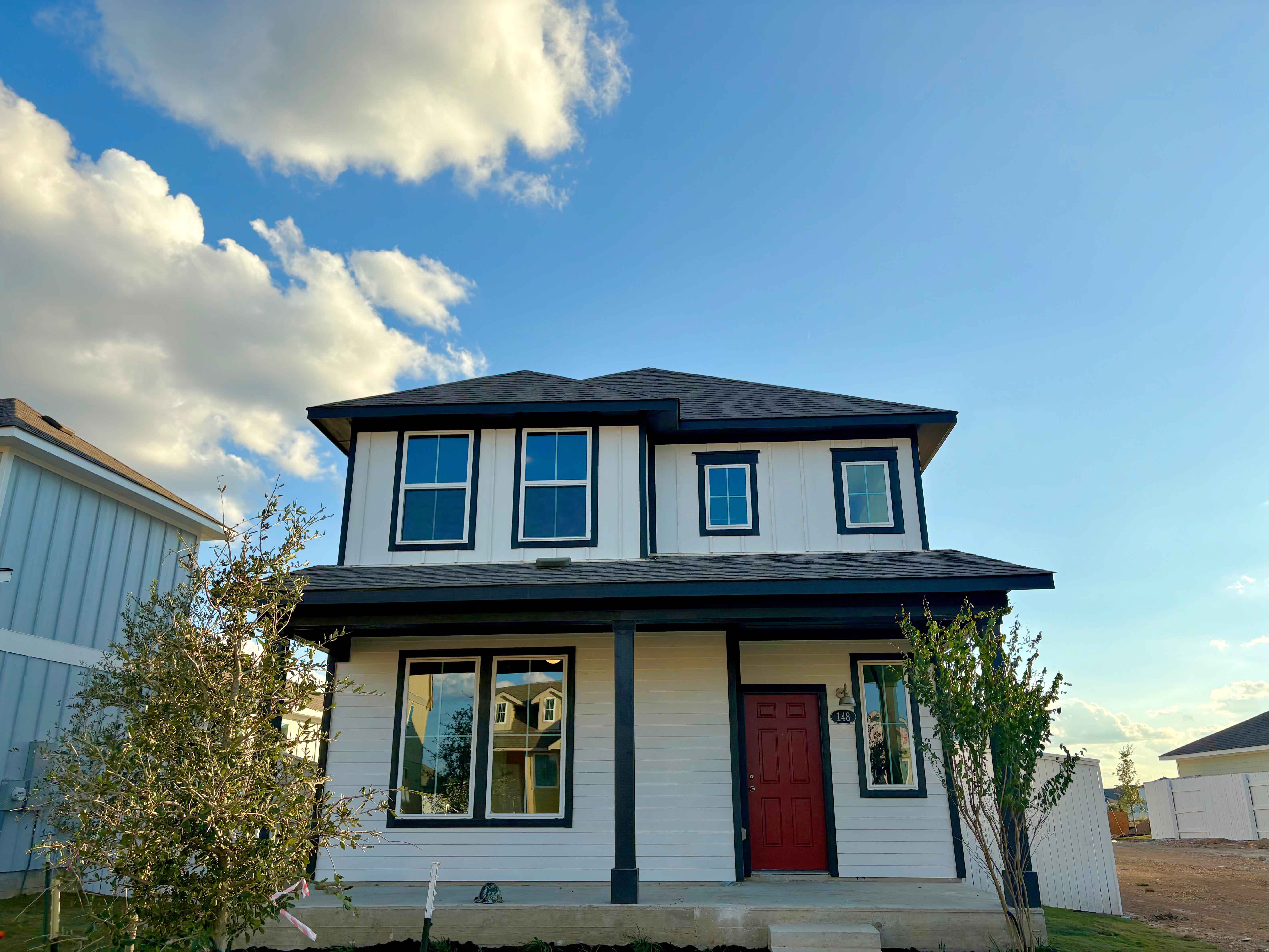 Image of the front of two-story white home framed with black with a red front door and the blue sky with clouds.