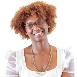 Headshot of woman with auburn curly hair, glasses, white blouse, and necklaces