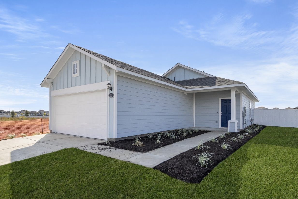 Image of a blue one story home with a dark blue door and a two car garage with a cement driveway with green grass and a blue sky