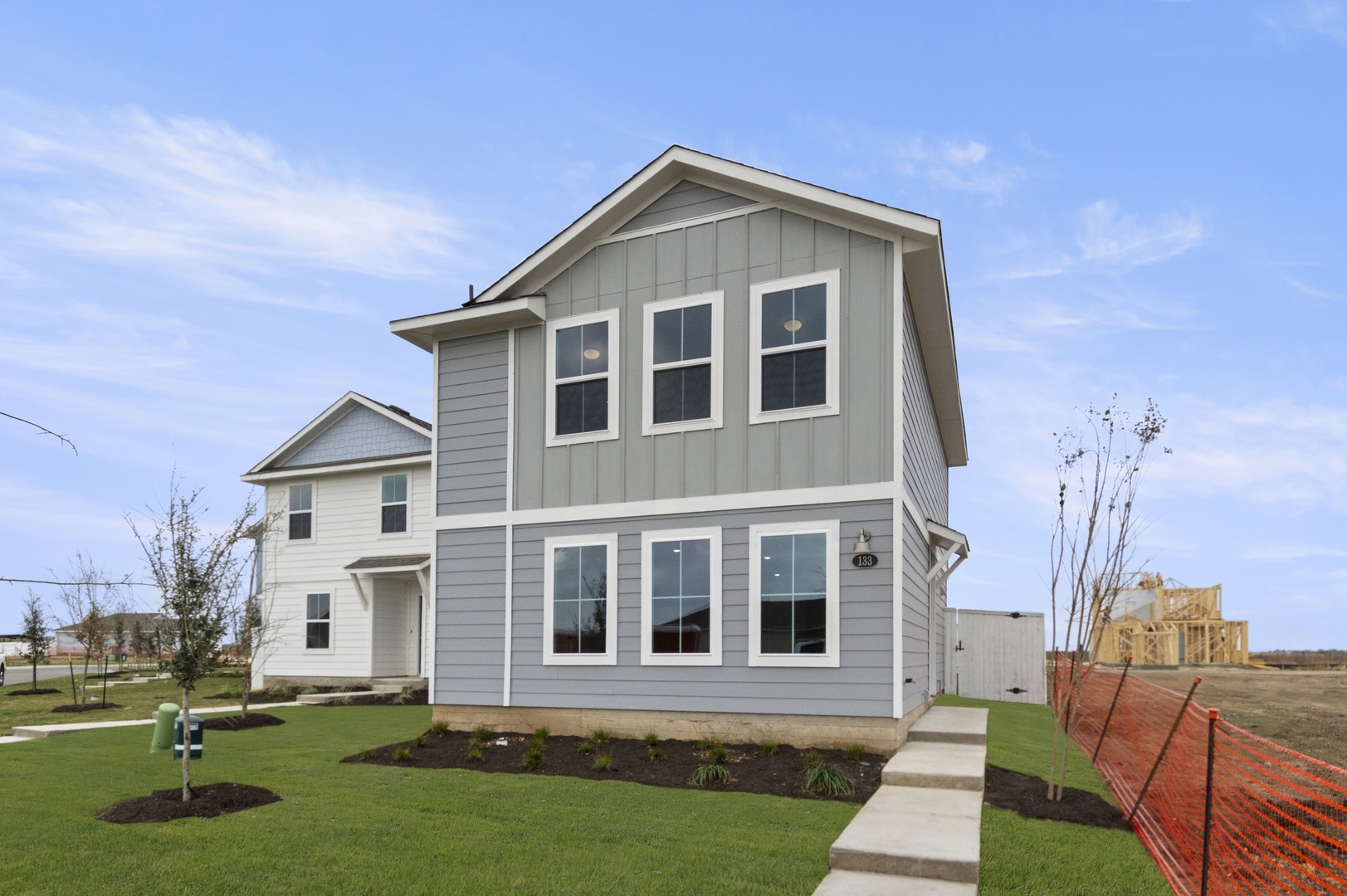 Image of a grey two story cottage home with a cement step walkway leading to the front door, green grass and a blue sky
