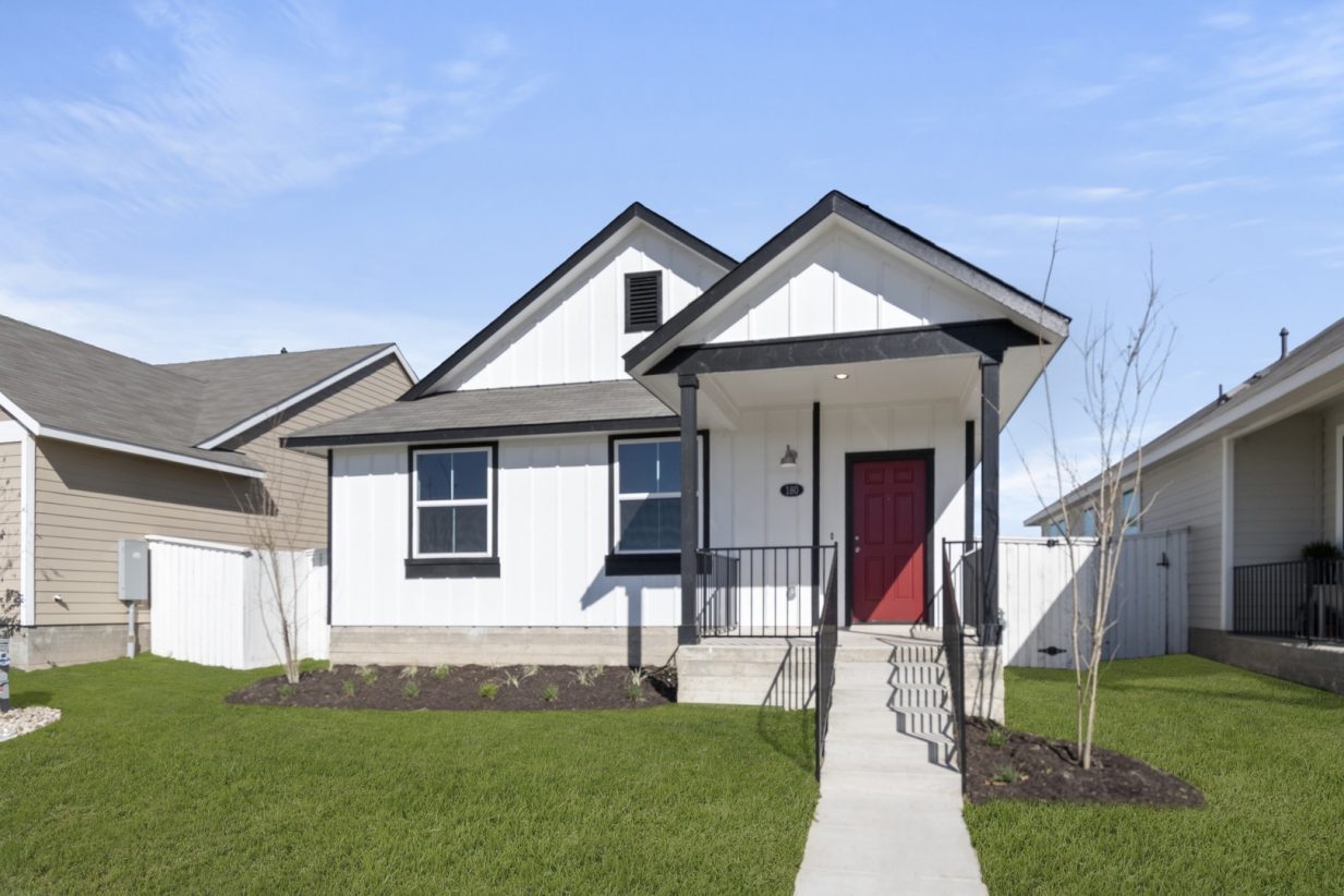 Image of a white one story house with black trim, a front patio, windows and a red front door