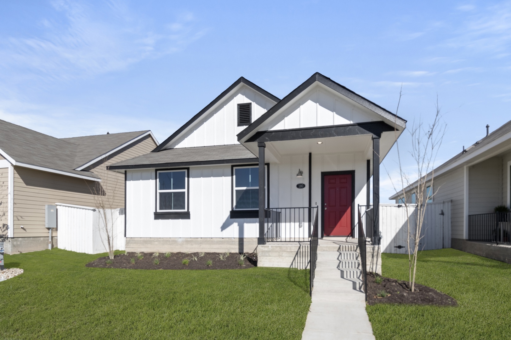 Image of a white one story house with black trim, a front patio, windows and a red front door