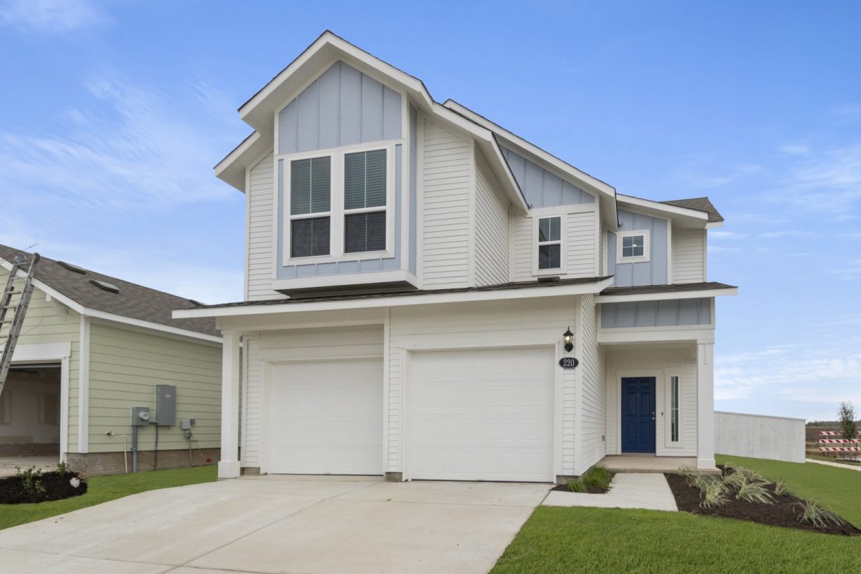 Image of the front exterior of a blue and white two-story home with a dark blue door, white two door garage, a cement driveway, and a clear blue sky