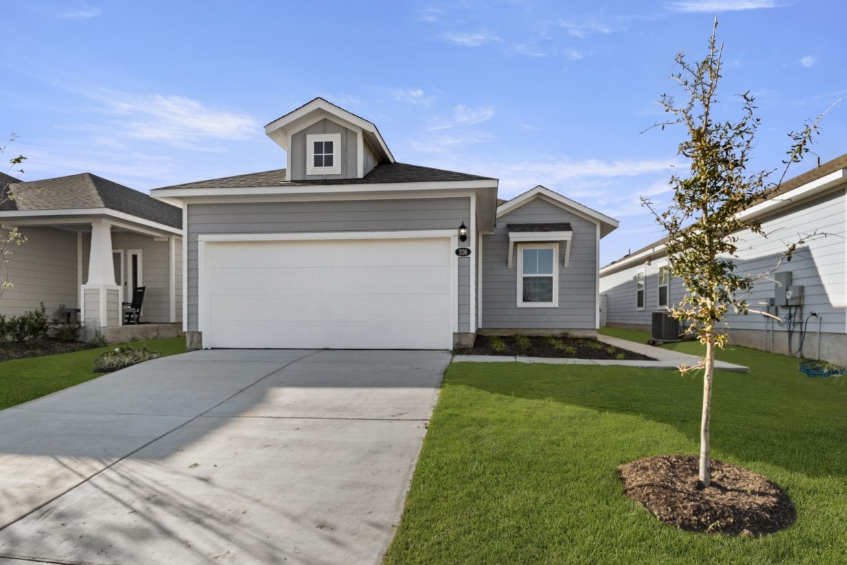 Image of a one story home with a two car garage and a cement driveway with green grass and a blue sky