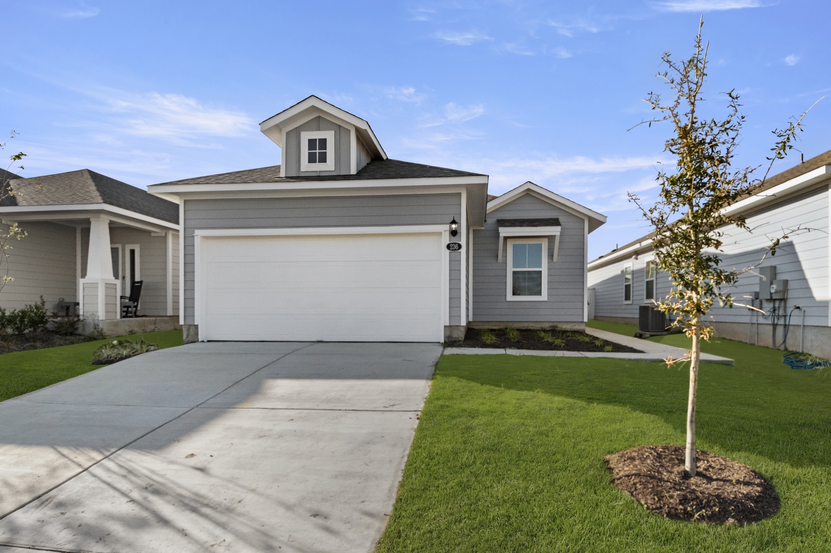 Image of a one story home with a two car garage and a cement driveway with green grass and a blue sky