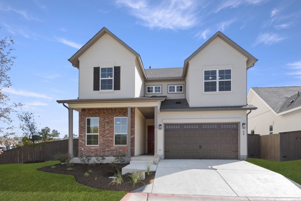 Image of a beige and brick two story home exterior with a brown garage and cement driveway with green grass and a blue sky