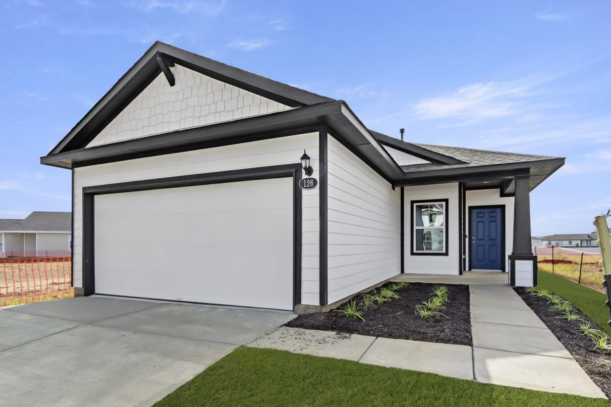 Image of the front of a white house with grey trim and a blue front door and a walkway with green grass