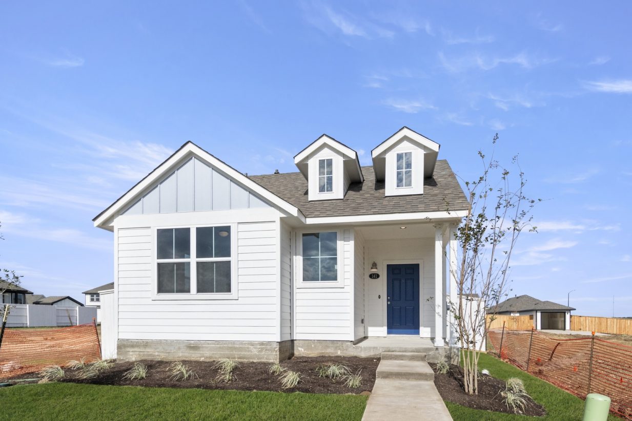 Front of blue one story home with blue door and green grass with a walkway