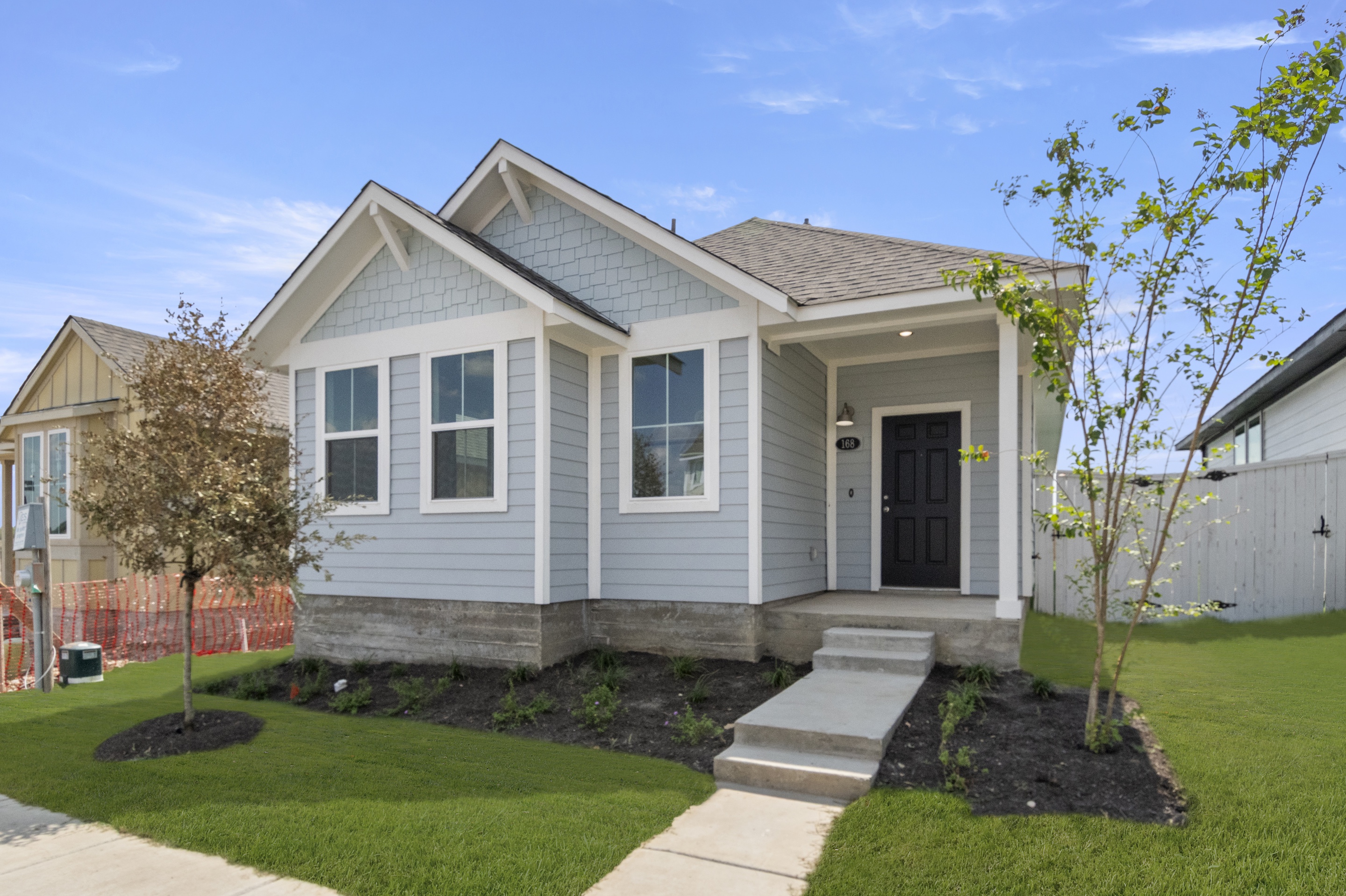 Image of front exterior of a blue one story house with white trim, a dark blue front door, green grass and a blue sky in the background