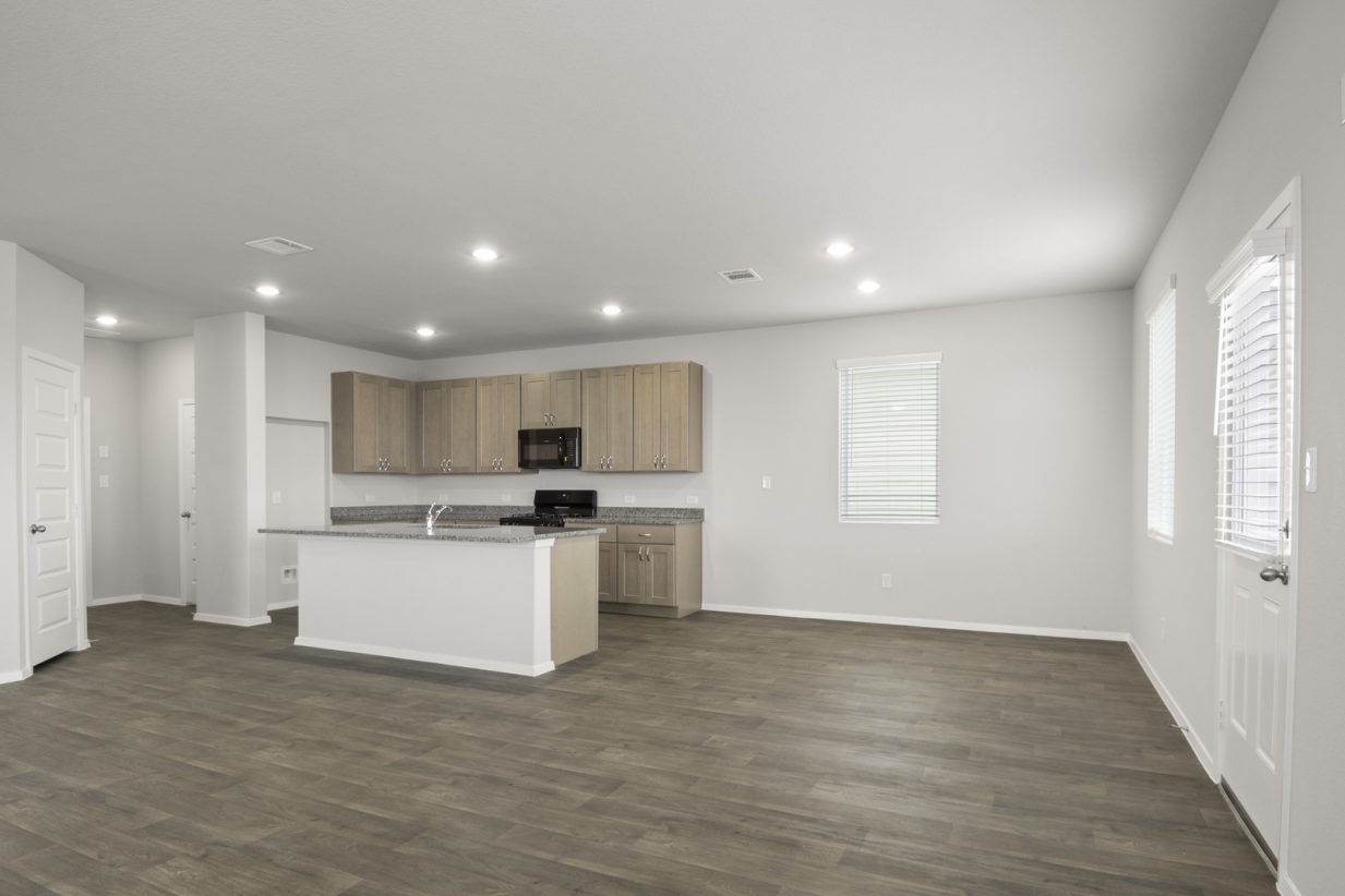 Image of a dining room with dark vinyl flooring and grey walls, and a L-shaped kitchen to the left