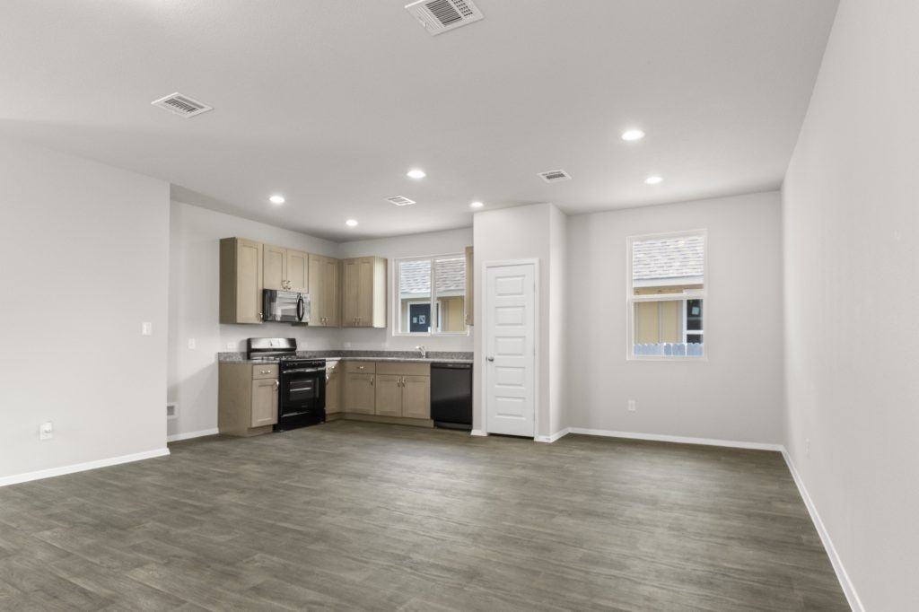 image of a dining room with a L-shaped kitchen with black appliances, granite countertops, and light brown cabinetry
