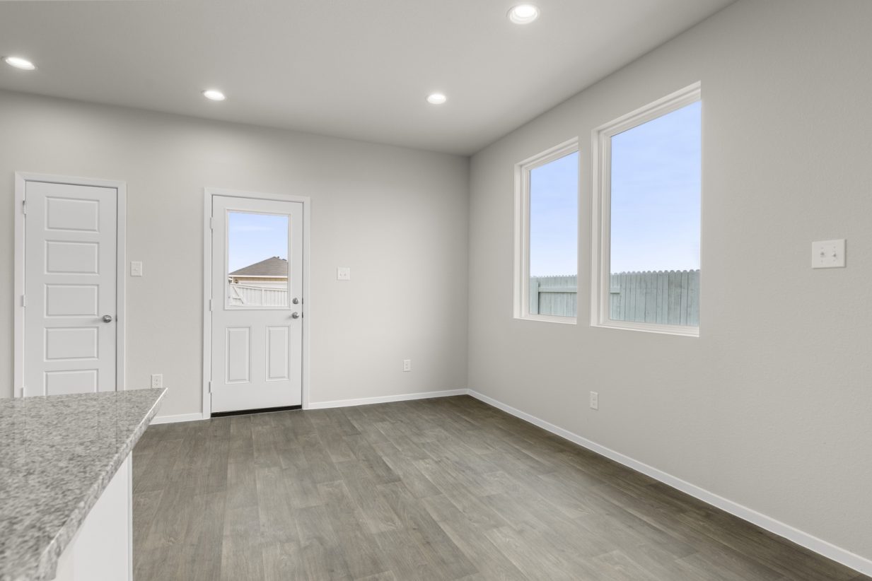 Image of a dining room area with cream walls, dark brown vinyl flooring, windows, and a white back door