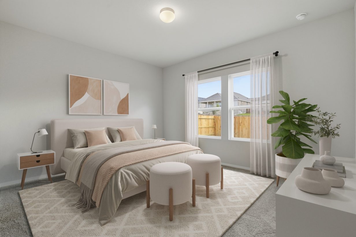 Image of a staged primary bedroom with a beige bed frame with earth tone bedding, a beige designed rug, a side table, wall decor, white curtains, and a green house plant