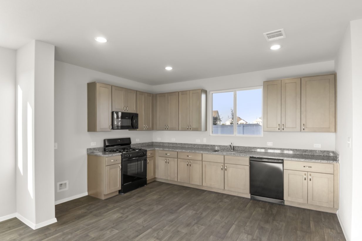 Image of a kitchen with brown cabinets, granite coutner tops, black appliances, and a window above the sink