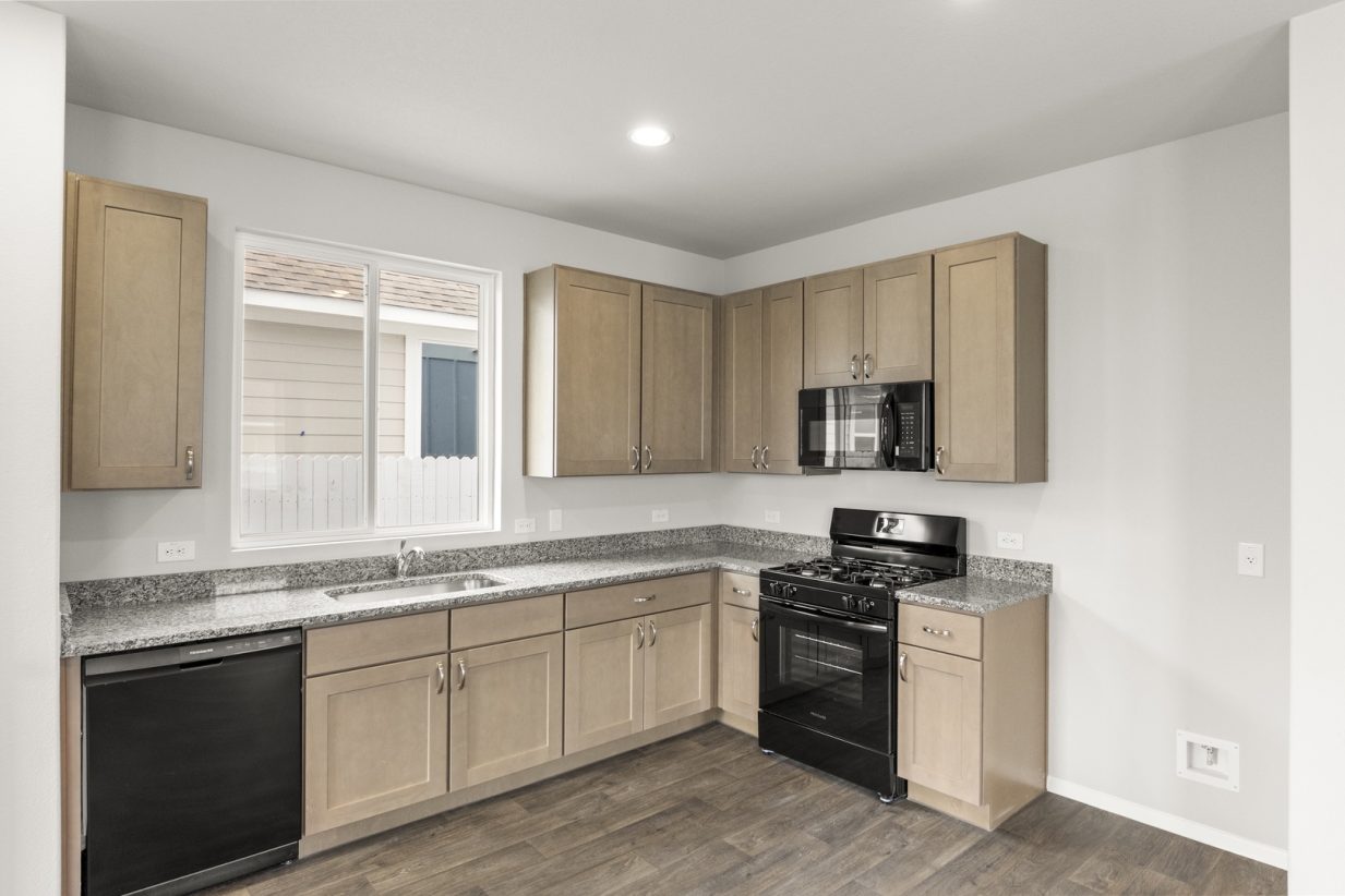 Image of a kitchen with light brown cabinets and black appliances with a window above the sink