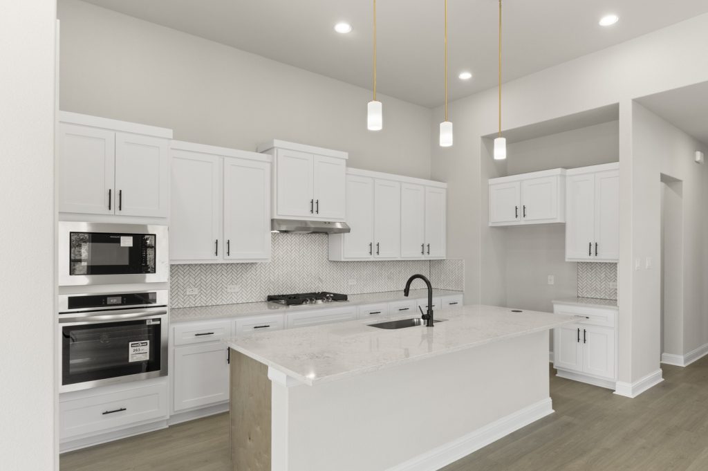 Image of a two story home kitchen with white cabinets, a center island, stainless steel appliances and white backsplash