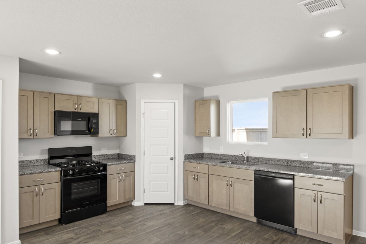 Image of a cottage home L-shaped kitchen with light brown cabinets, granite countertops and black kitchen appliances with a window above the sink
