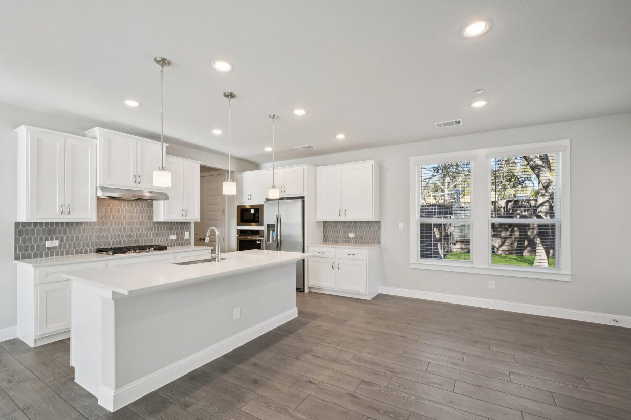 Image of a kitchen and dining room area with white cabinets, a white center island, stainless steel appliances and windows
