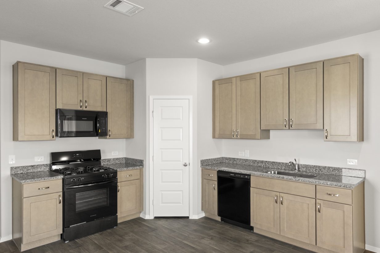 Image of kitchen with light brown cabinets with black appliances and grey countertop
