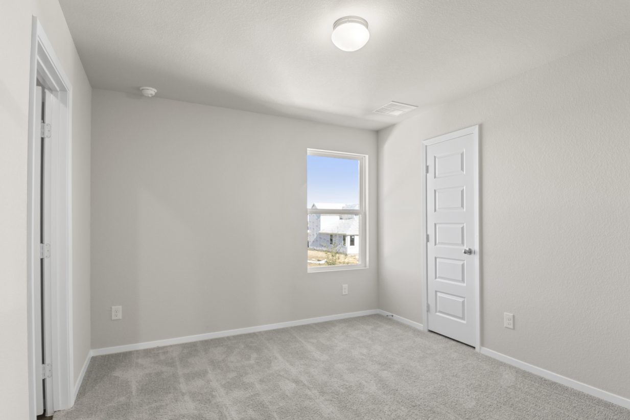 Image of a primary bedroom with tan carpeting, light grey walls, a white bathroom door and a window