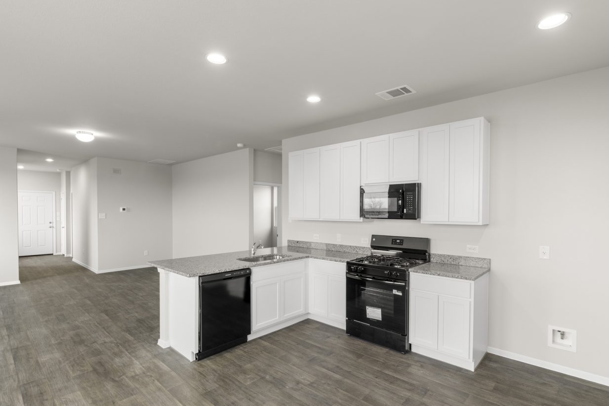 Image of an L-shaped kitchen with white cabinets, black appliances and granite countertops