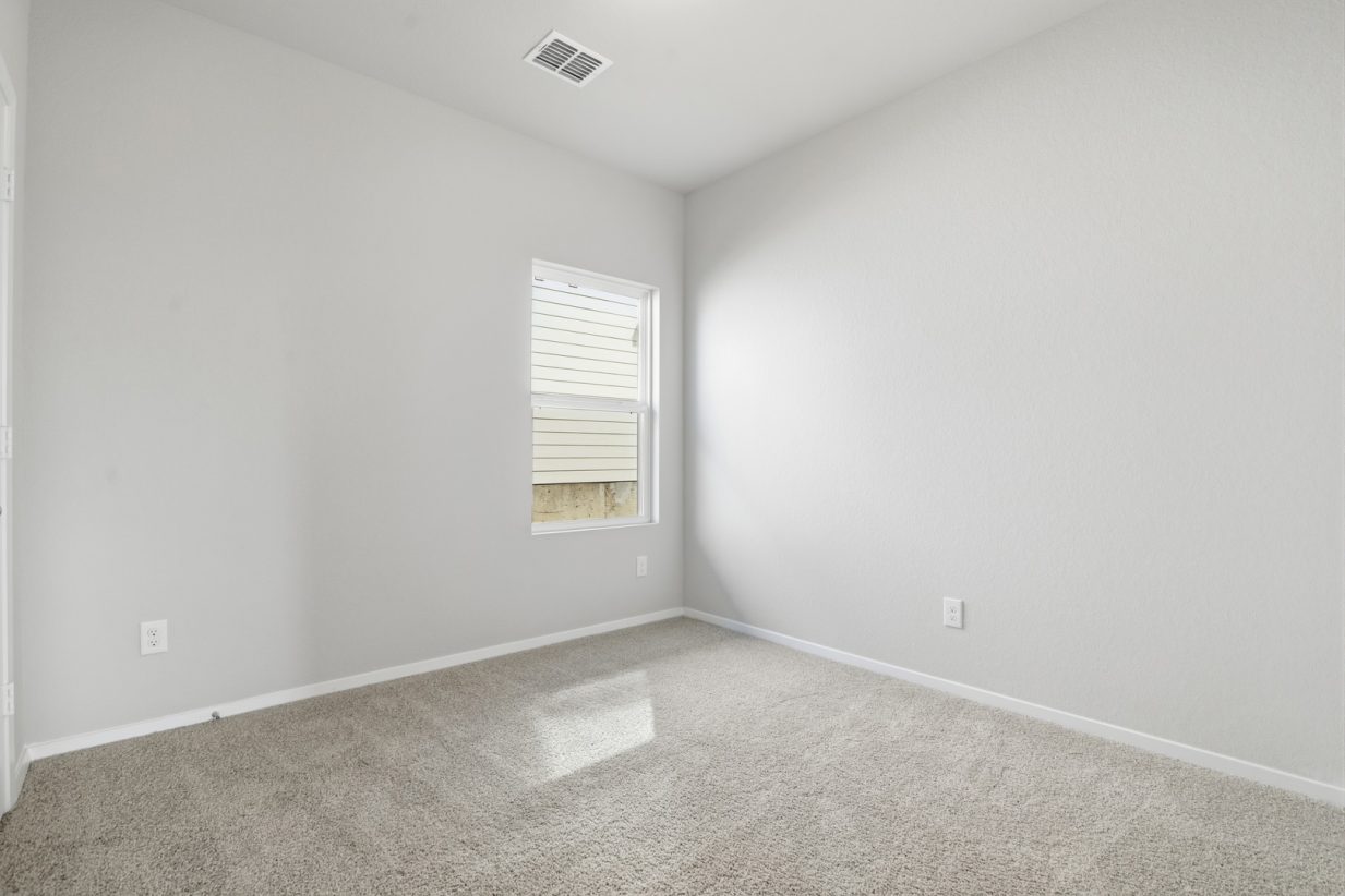Image of a bedroom with tan carpeting, light grey walls, a window and white trim