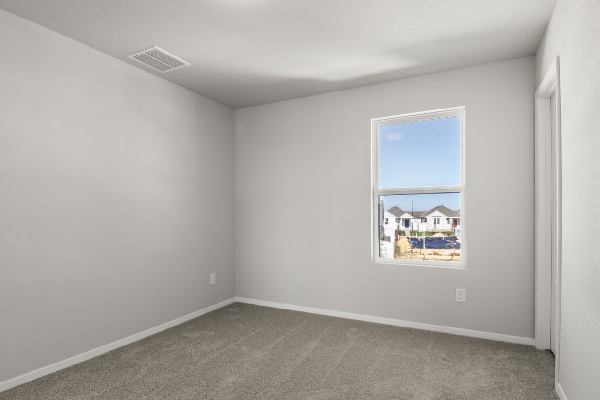 Image of a primary bedroom with light grey walls, tan carpeting and a window