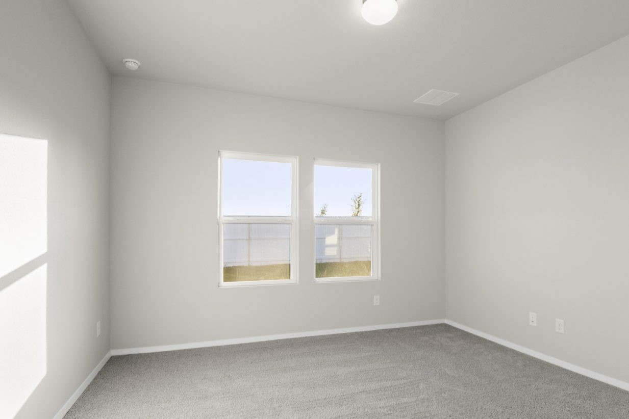 Image of a one story home bedroom with tan carpeting and light grey walls with two windows