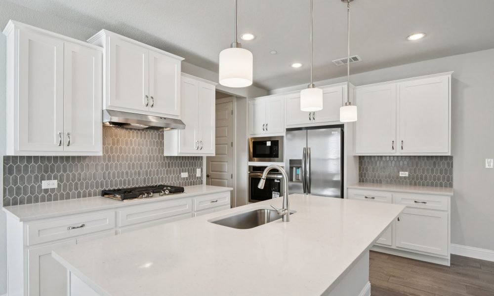 Image of a kitchen with white cabinets, a center island, stainless steel appliances, and dangling lights
