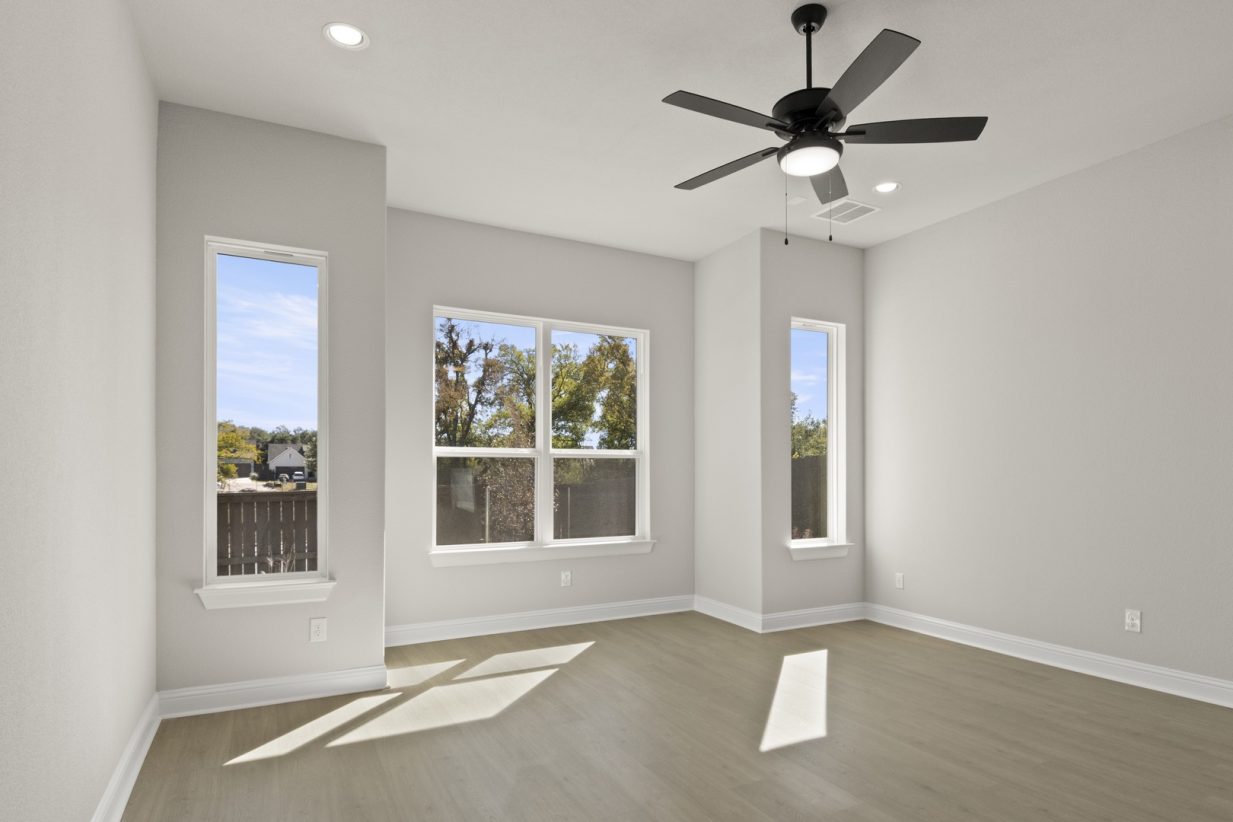 Image of two story home bedroom with light brown wooden flooring and light grey painted walls with windows