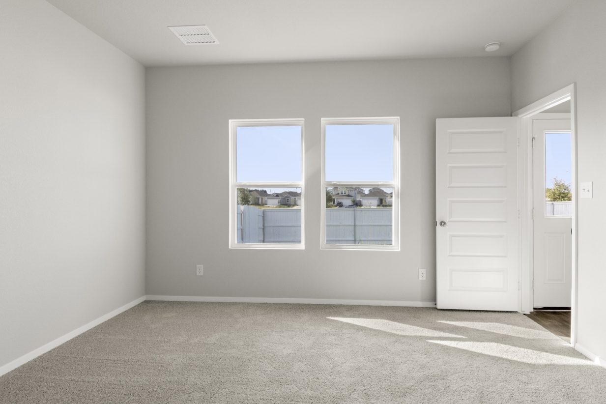 Image of primary bedroom with tan carpet and light grey walls and two windows
