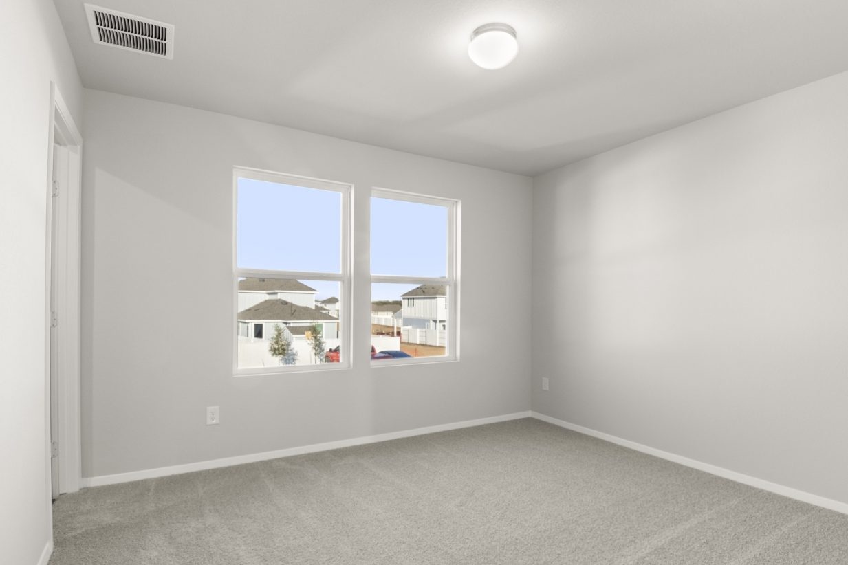 Image of a bedroom with tan carpeting and light grey painted walls with two windows
