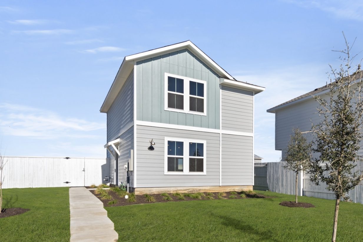 Image of the front exterior of a light blue two story cottage home with windows, white trim, a cement walkway to front door, green grass and a blue sky in the background