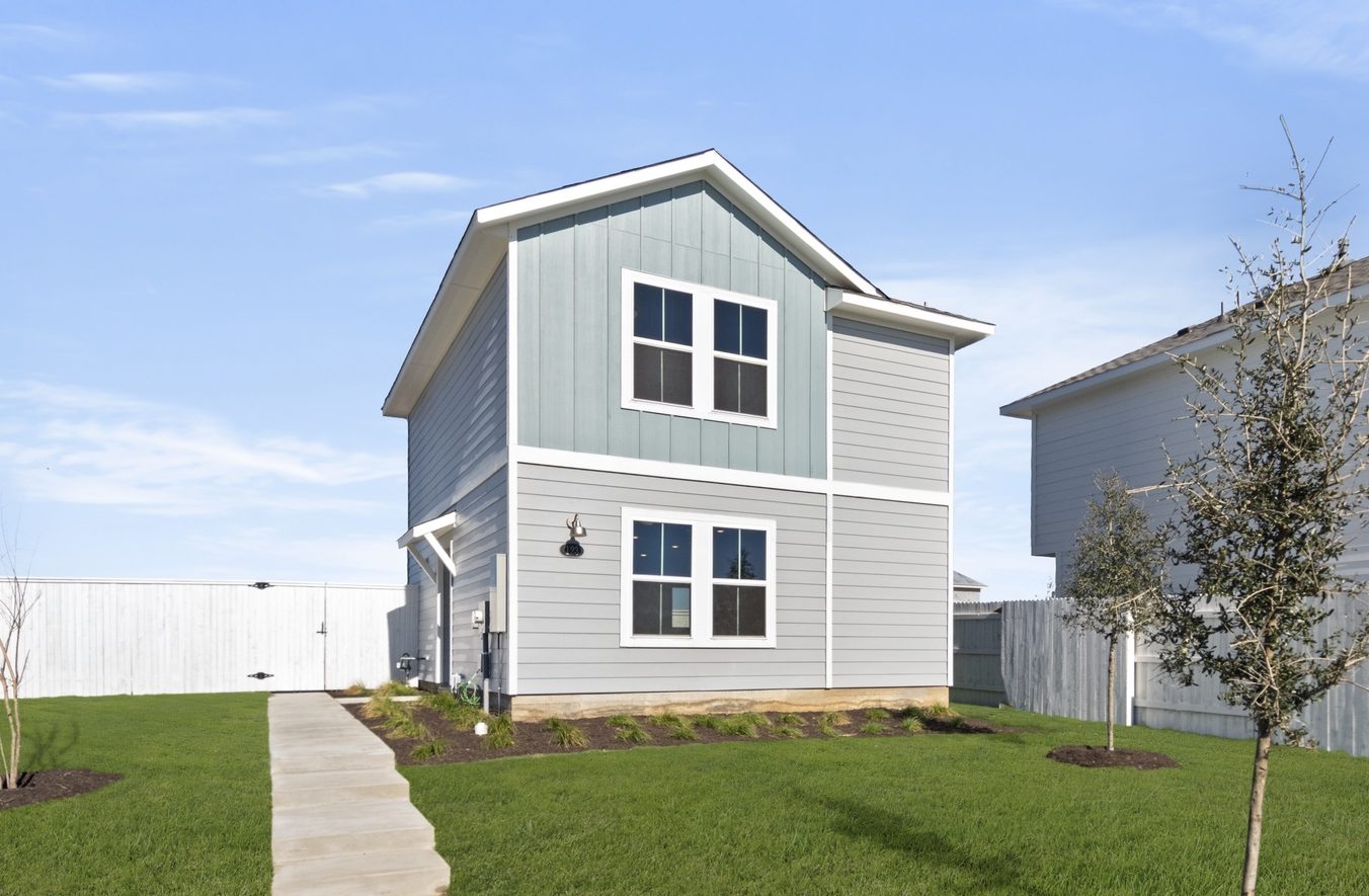 Image of the front exterior of a light blue two story cottage home with windows, white trim, a cement walkway to front door, green grass and a blue sky in the background