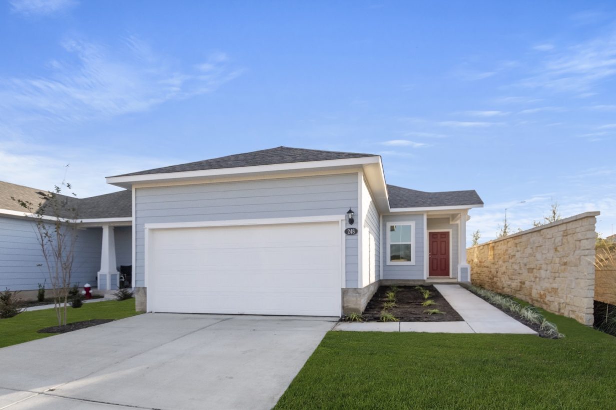 Image of exterior grey one story home with a red door and white two car garage with a cement driveway and a blue sky