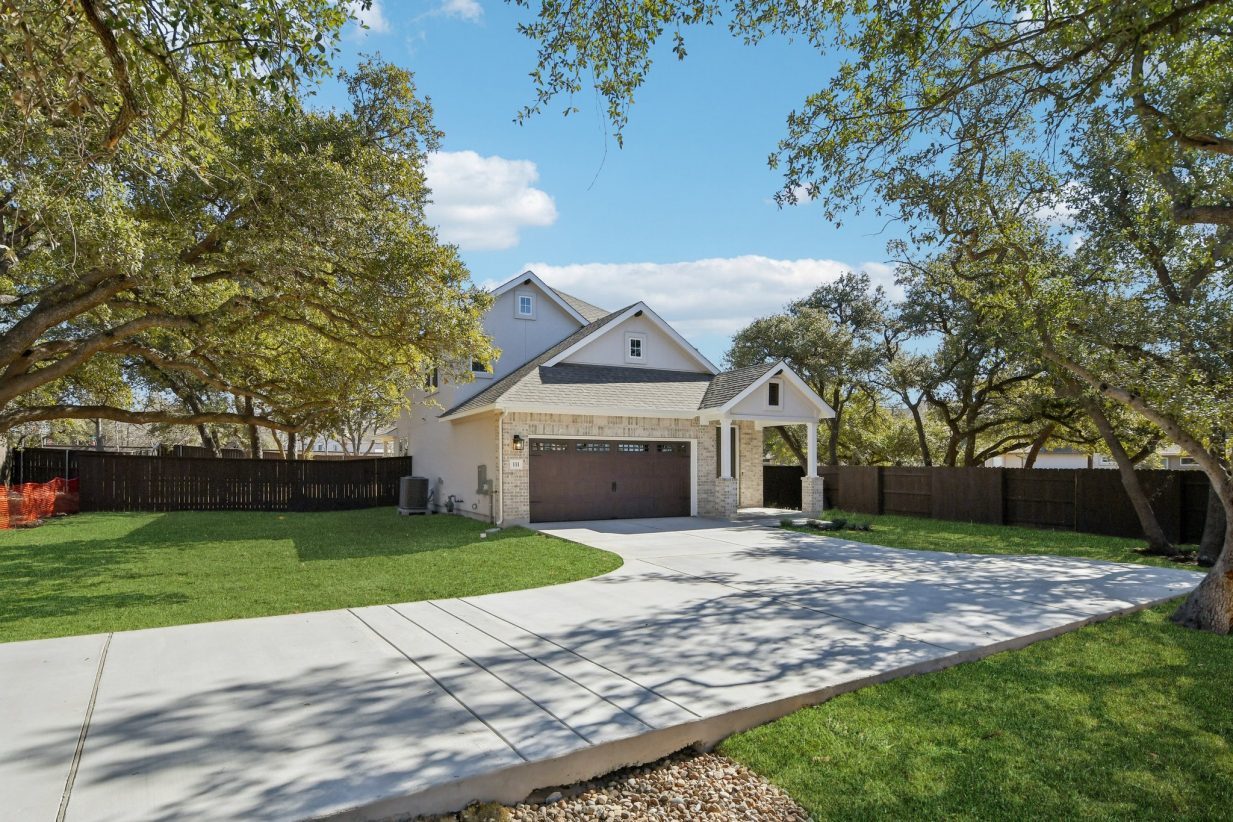 Image of a brick two story house with a brown garage door and front door, beige brick, green grass, and a blue sky in the background