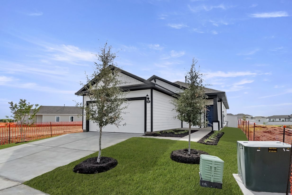 Image of the front yard of a white house with grey trim and a blue door
