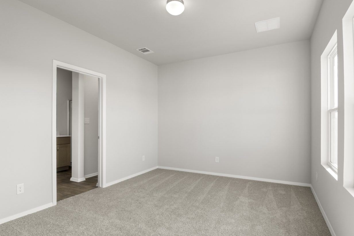 Image of primary bedroom with tan carpet and light grey walls with a connecting bathroom