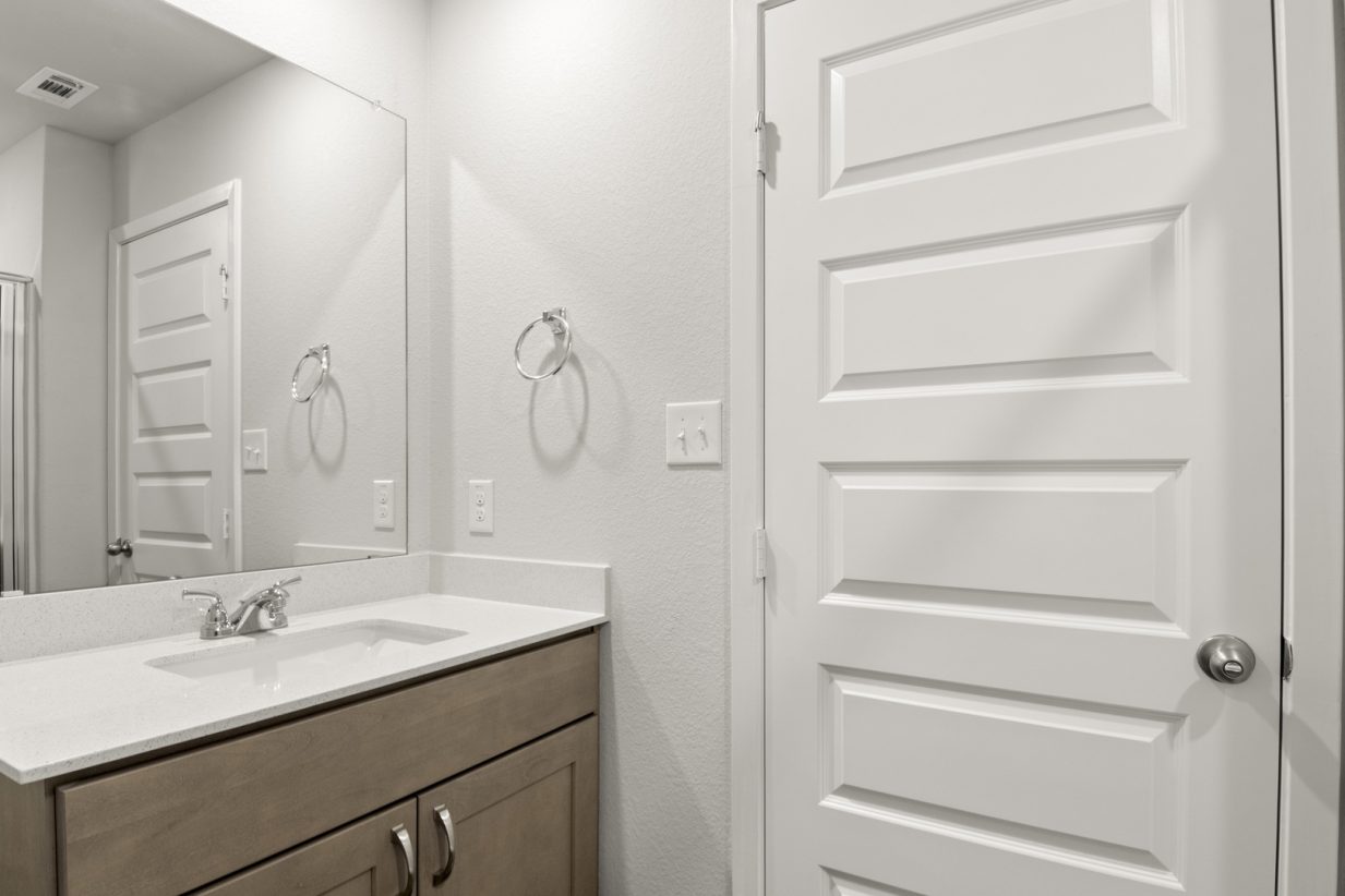 Image of a bathroom with a white vanity and a large mirror and brown cabinets