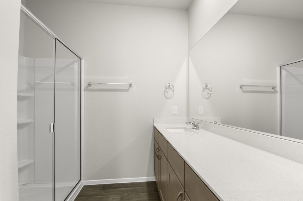 Image of a bathroom with brown wood-like flooring and white vanity with mirror and a walk-in shower